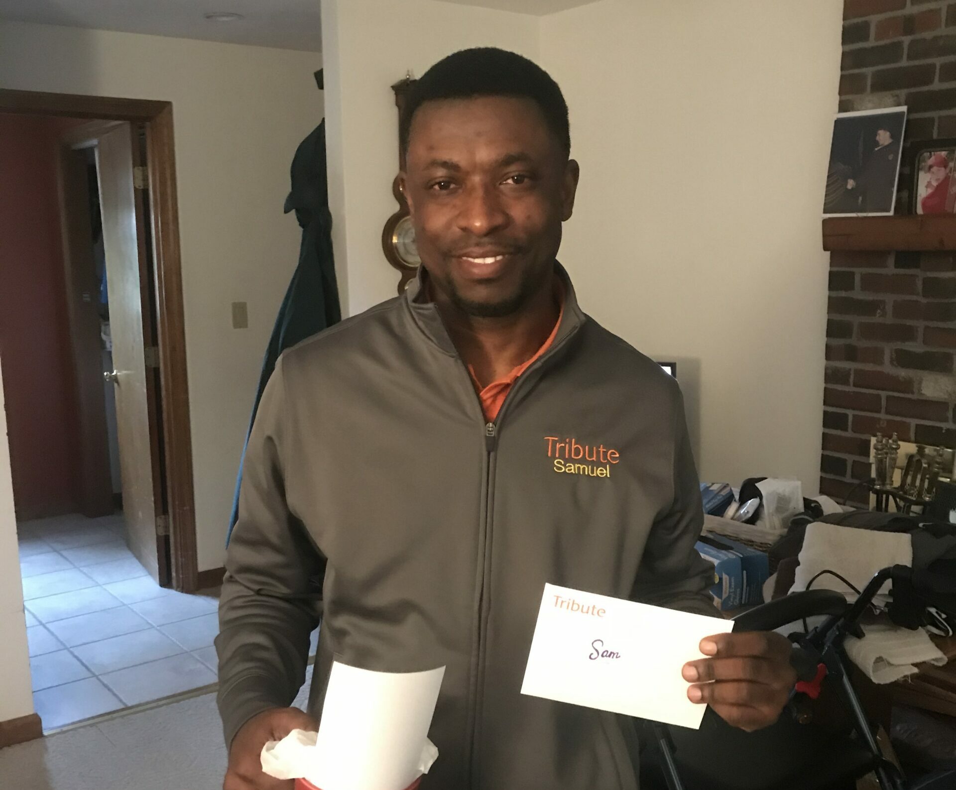 Tribute Caregiver Samuel smiles holding gift and card from Tribute Home Care