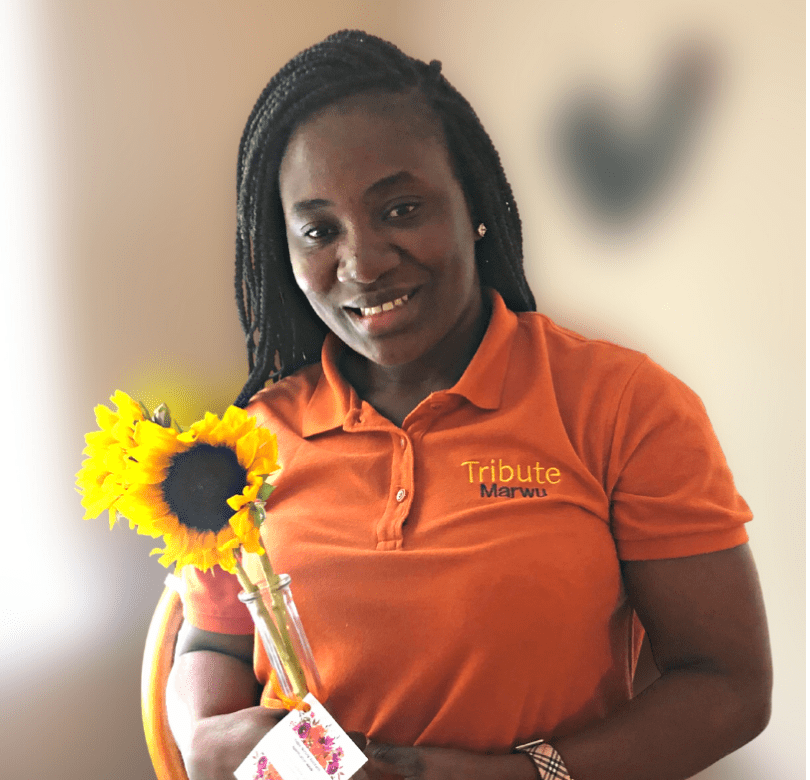 Tribute Caregiver Marwu smiling with flowers from Tribute Home Care