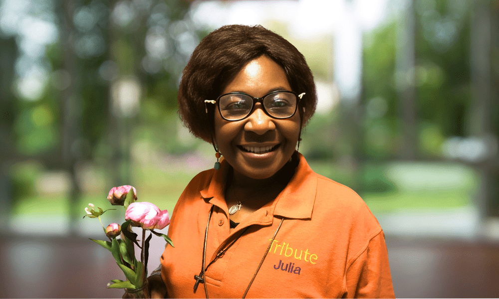 Tribute Caregiver Julia smiling in Tribute Home Care uniform holding flowers