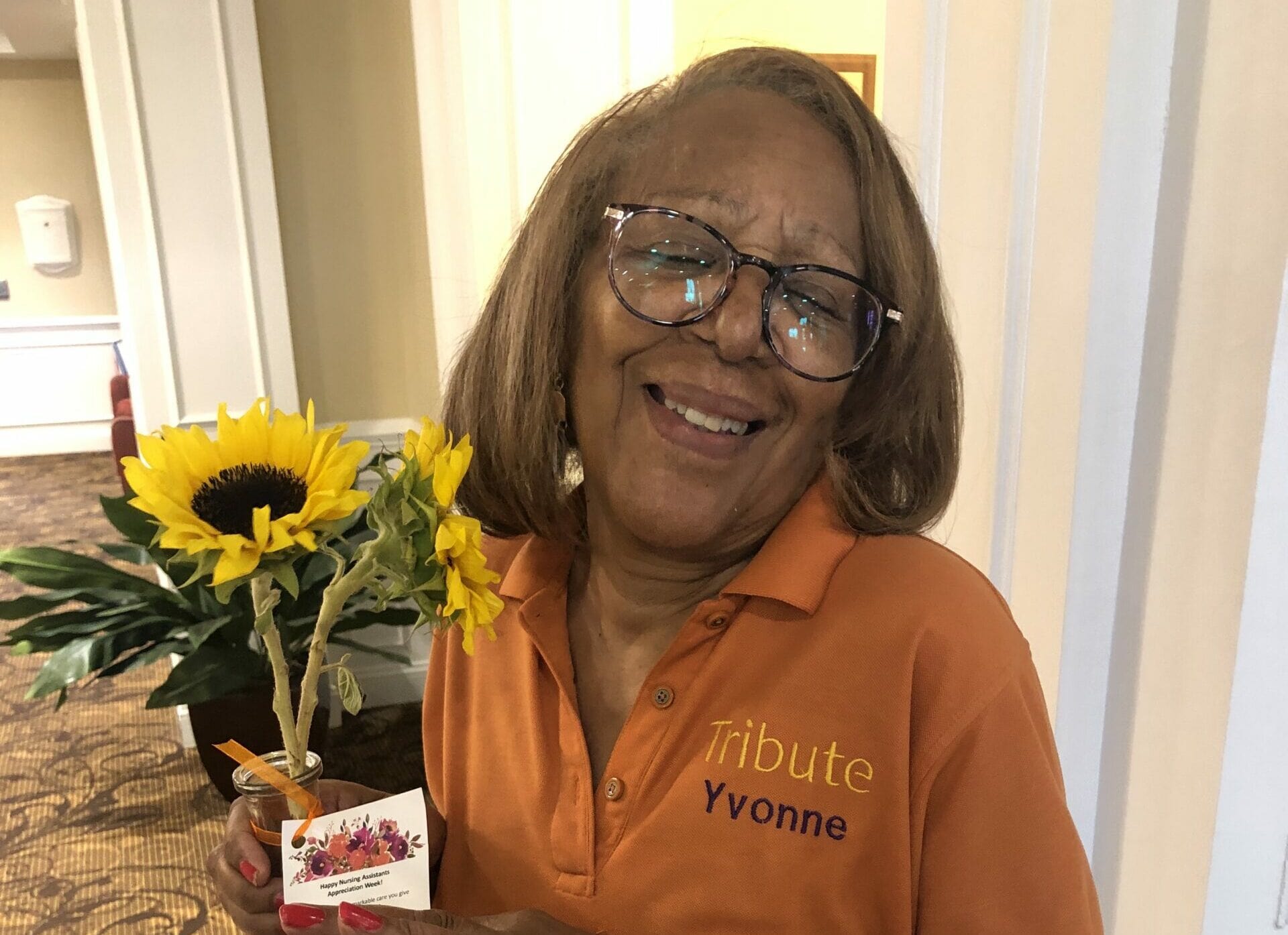 Tribute Caregiver Yvonne smiling in Tribute Home Care uniform holding sunflowers