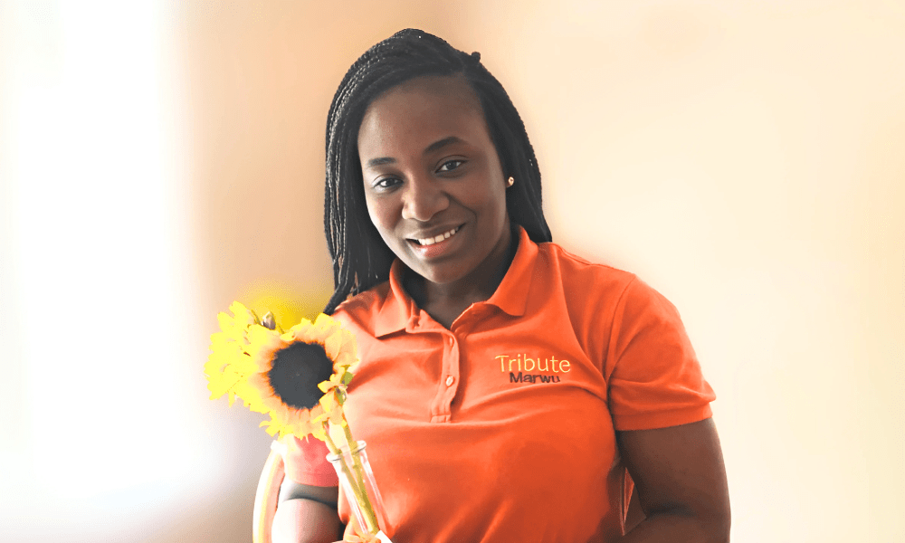 Tribute Caregiver Marwu smiling in Tribute Home Care uniform holding sunflowers